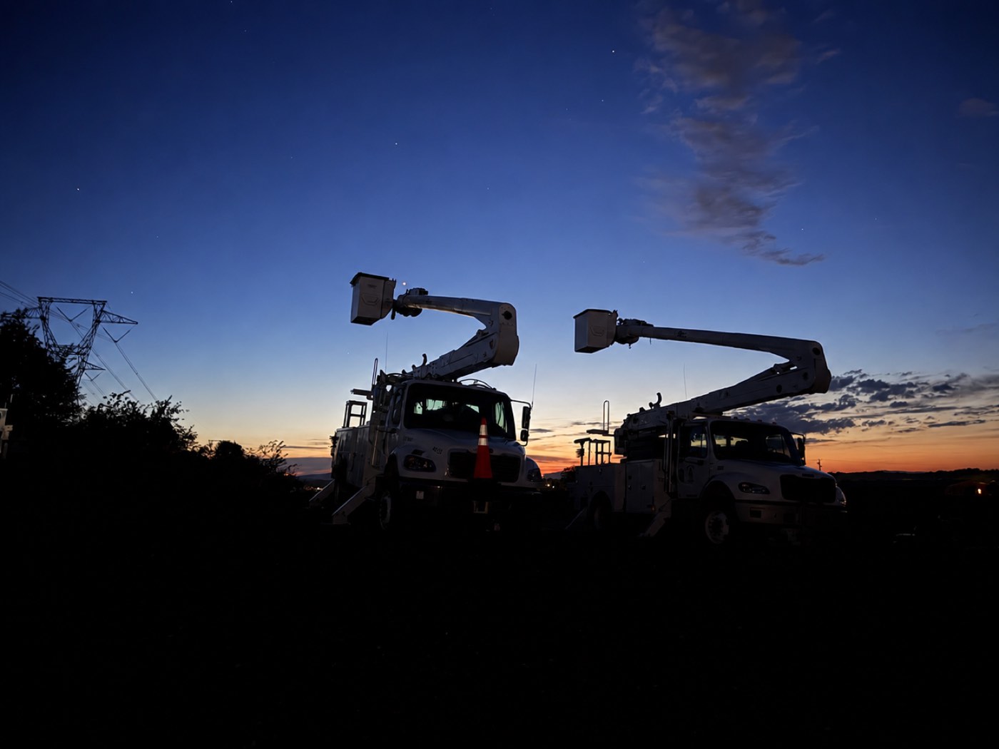 Two bucket trucks at sunset